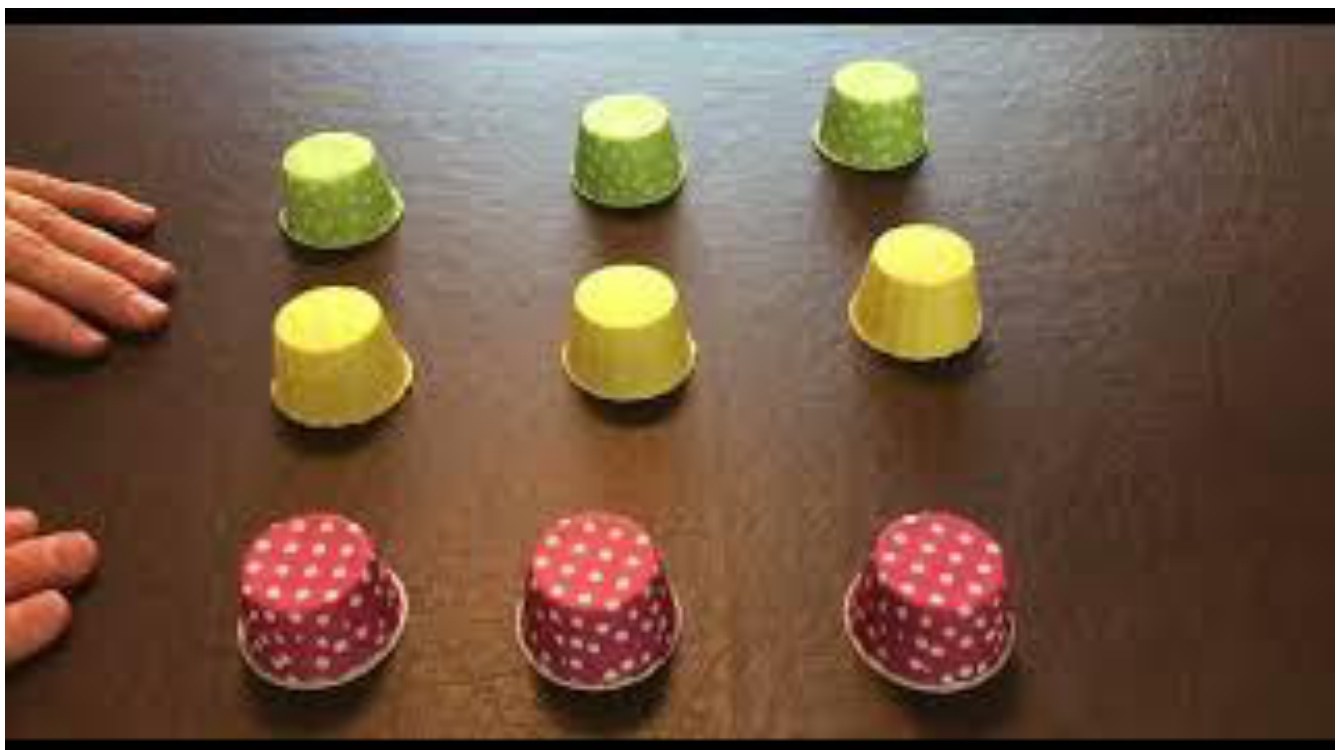 Three red cups in the foreground, green and yellow cups behind, on a wooden table